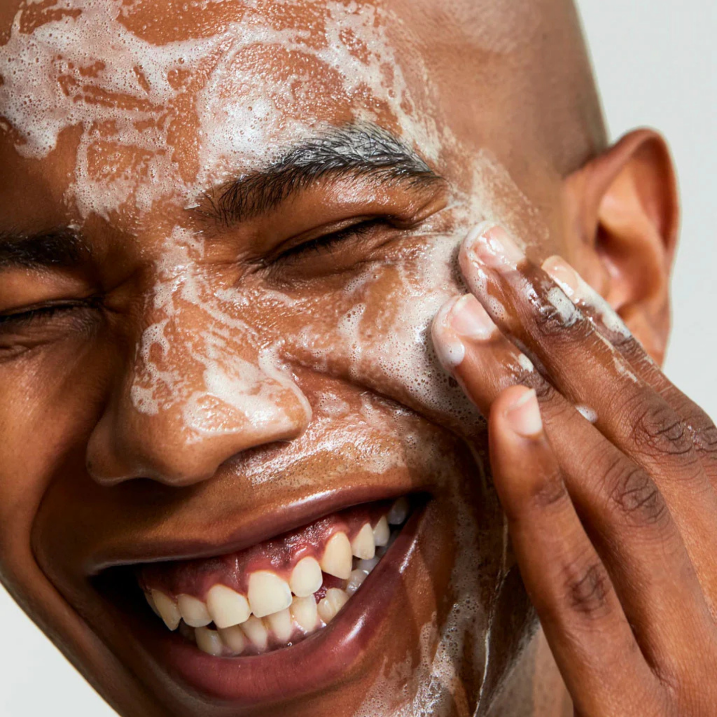 Man washing his face with AXIS-Y Quinoa One-Step Balanced Gel Cleanser to their face with a neutral background. He is smiling and happy
