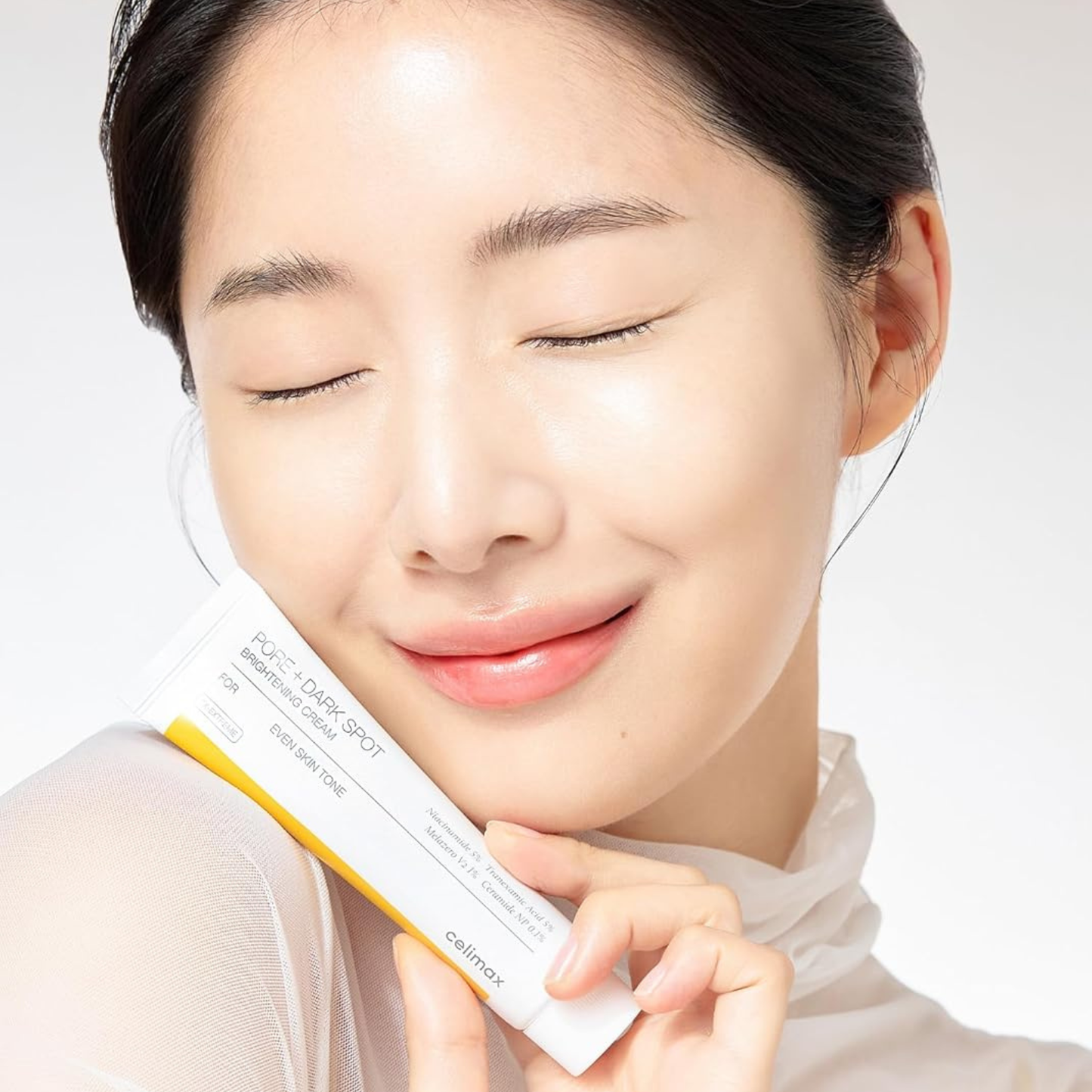 woman holding Celimax Pore+Dark Spot Brightening Cream and smiling with her eyes closed