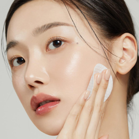 Woman applying Medicube Zero Pore Pad 2.0 to her face with a neutral background