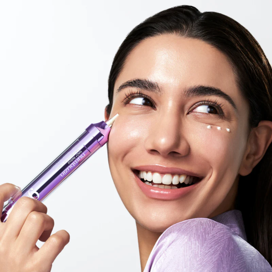 Woman smiling and holding a tube of Numbuzin No.9 NAD+ Retinol Volumetox Eye Cream. She has three cream dots applied under her eye area