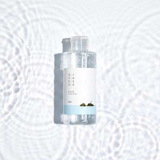 Clear bottle ROUND LAB 1025 Dokdo Toner with a label on a water textured white background
