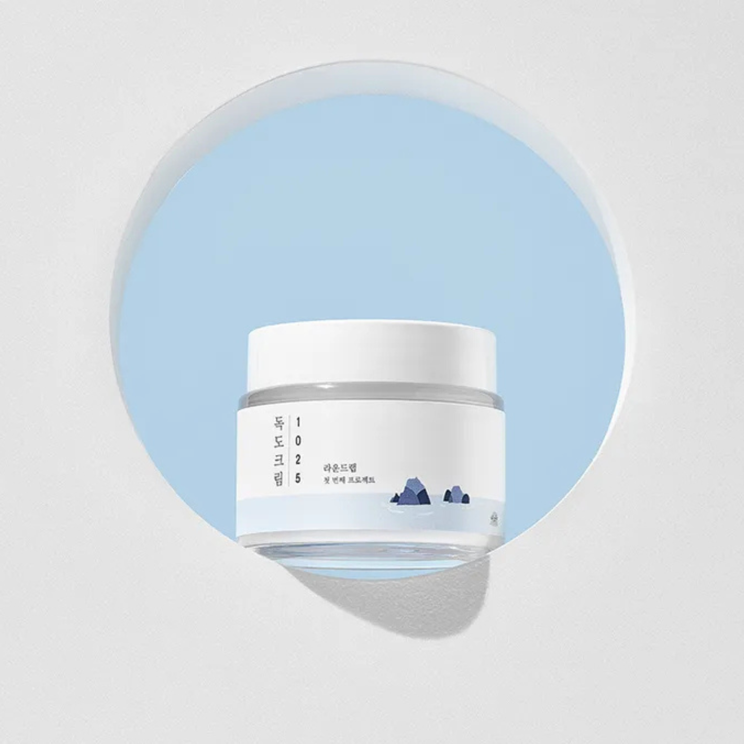 White jar of Round Lab 1025 Dokdo Cream with blue label on a light gray background