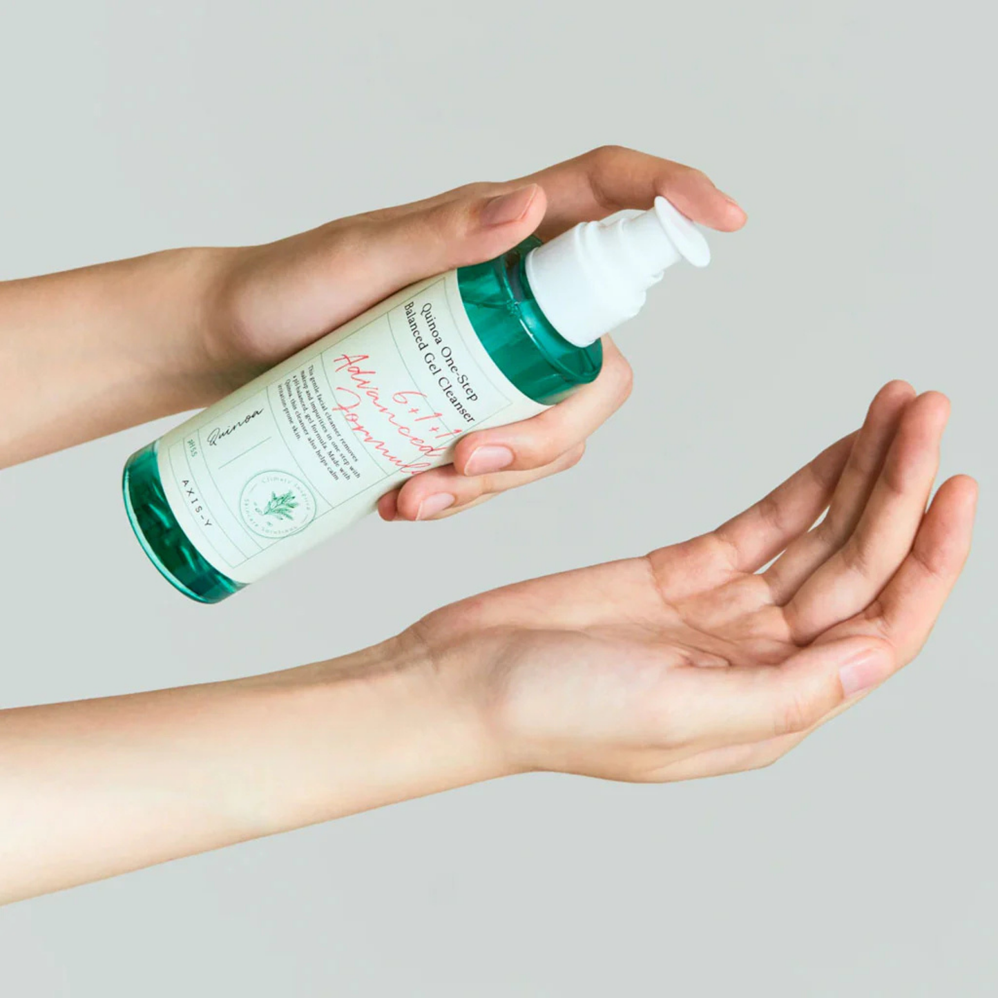 Person holding a bottle oAXIS-Y Quinoa One-Step Balanced Gel Cleanser with a pump on a light gray background