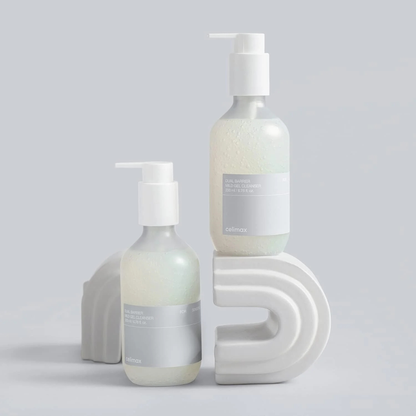 Two bottles of CELIMAX Dual Barrier Mild Gel Cleanser on a grey background with rainbow shaped platforms