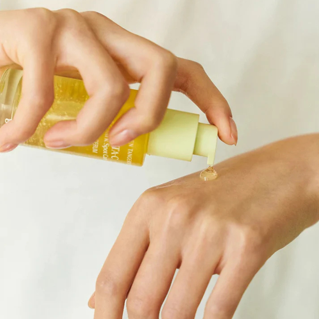 Hand  holding a bottle of Goodal Green Tangerine Vita‑C Dark Spot Care Serum and dispensing a droplet on the other hand