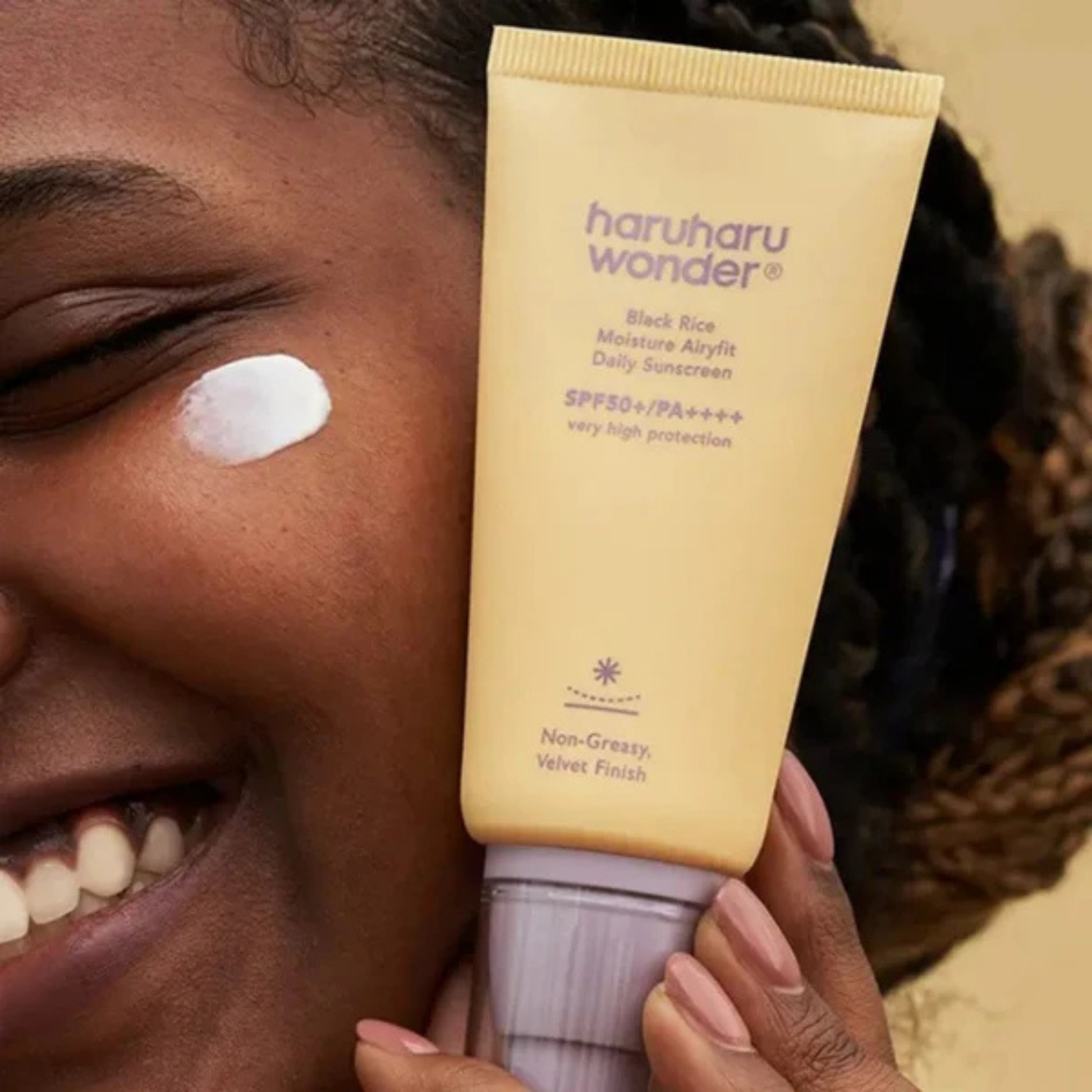 Close up of a woman holding a tube of Haruharu Wonder Black Rice Moisture Airyfit Daily Sunscreen SPF50 with some sunscreen on her cheek