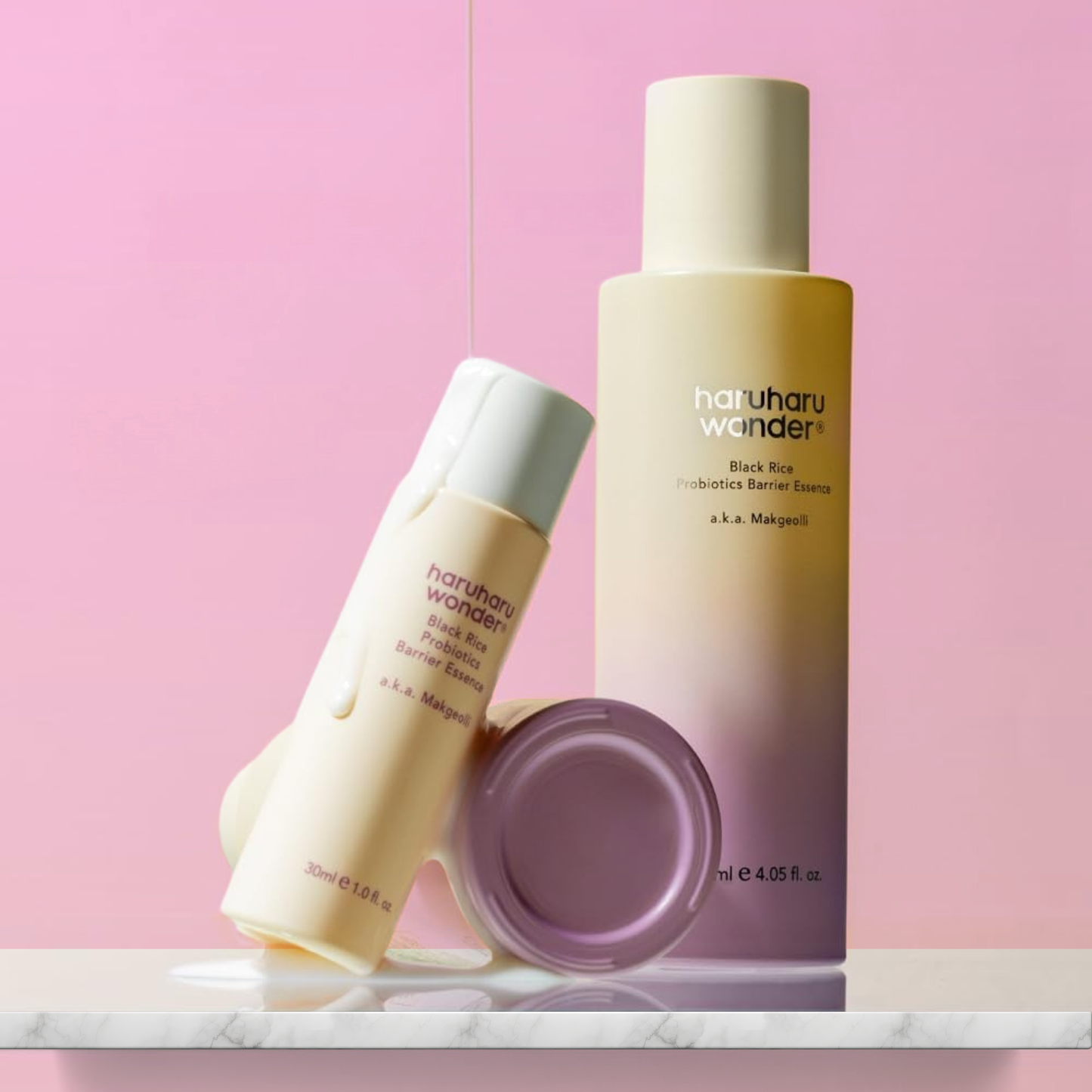 Two skincare bottles of Haruharu Wonder Black Rice Probiotics Barrier Essence on a pink background