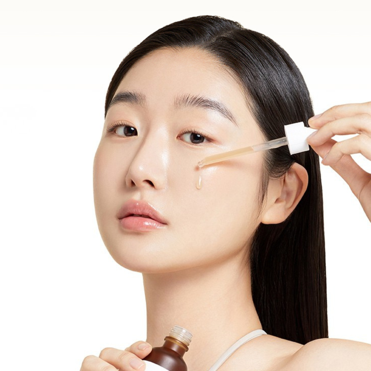 Woman applying Ma:nyo Bifida Biome Complex Ampoule with a dropper to her cheek on a white background