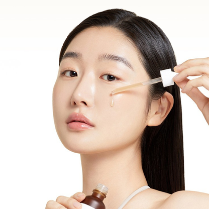 Woman applying Ma:nyo Bifida Biome Complex Ampoule with a dropper to her cheek on a white background