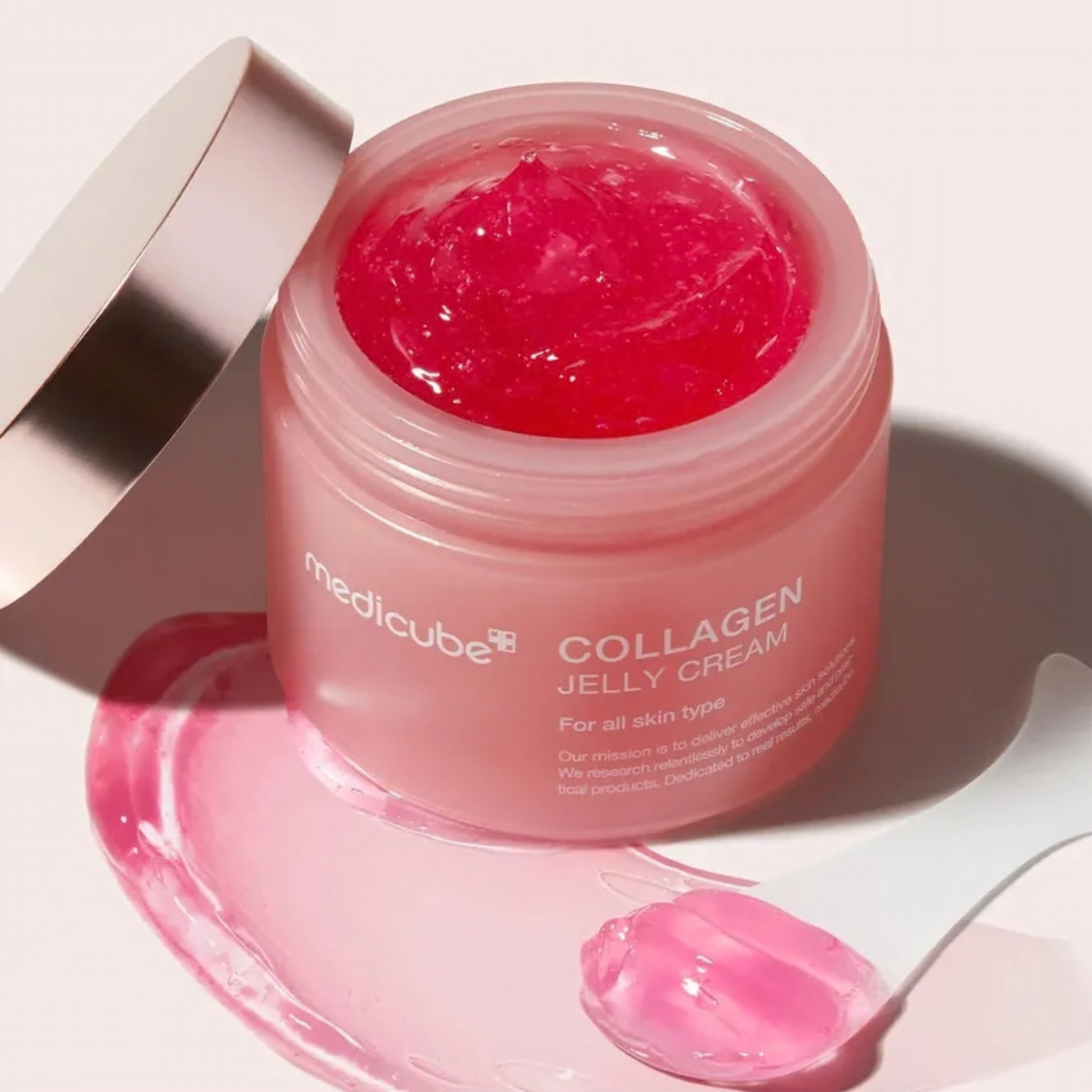 Pink jar of Medicube Collagen Jelly Cream on a light background with a scoop and jelly-cream smear.