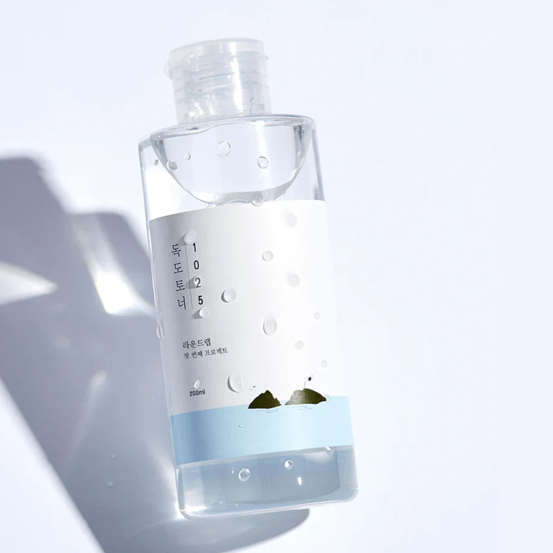 Clear bottle ROUND LAB 1025 Dokdo Toner with a label on a light gray background