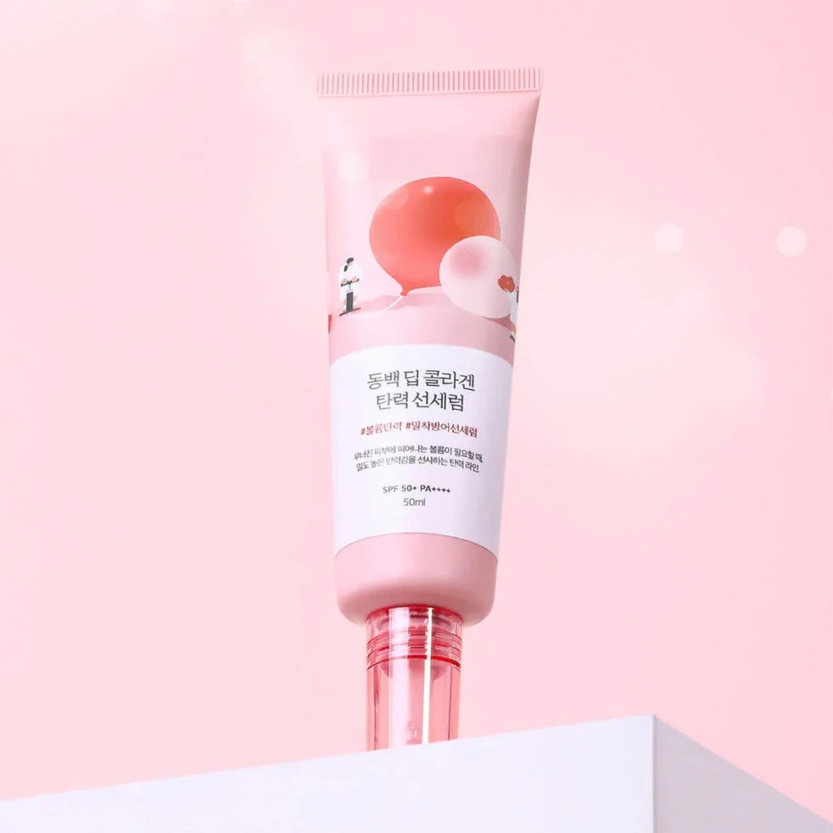 ROUND LAB Camellia Deep Collagen Firming Sun Serum on a platform with a pink background