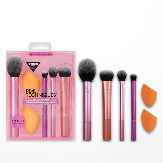 A collection of Real Techniques makeup brushes and a bonus complexion sponge, displayed in front of their packaging which is predominantly pink with product images on the cover.
