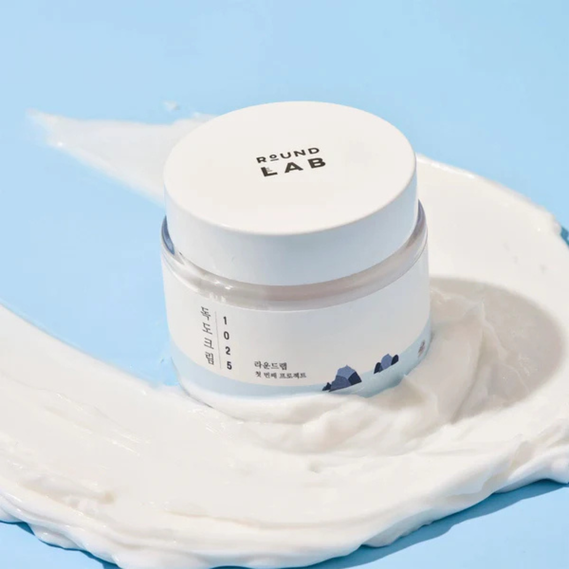 Jar of Round Lab 1025 Dokdo Cream with a white lid on a light blue background