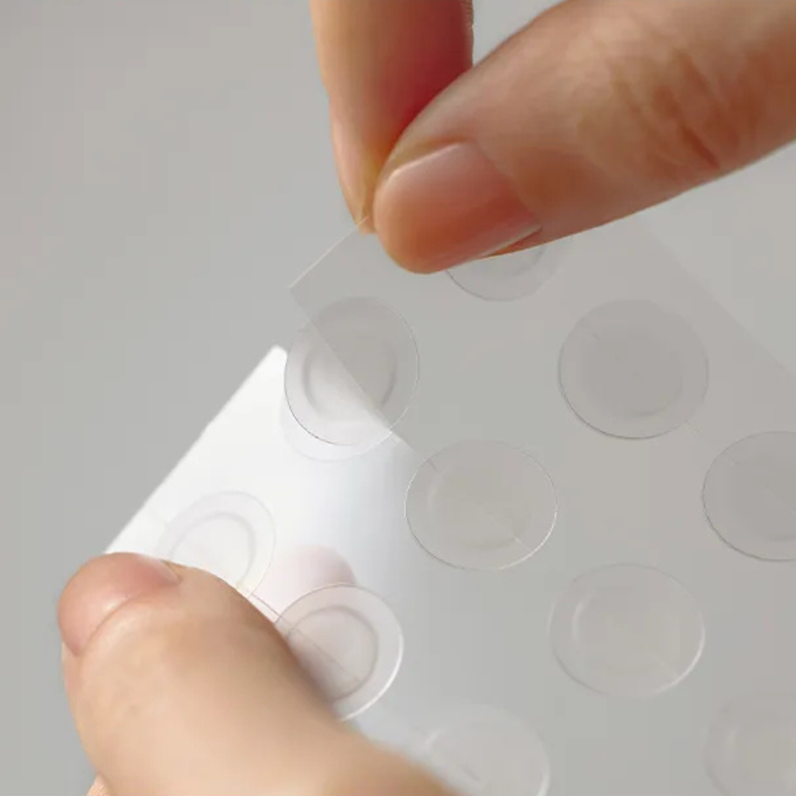 Hand holding a sheet of SOME BY MI 30 Day Miracle Clear Spot Patches against a gray background