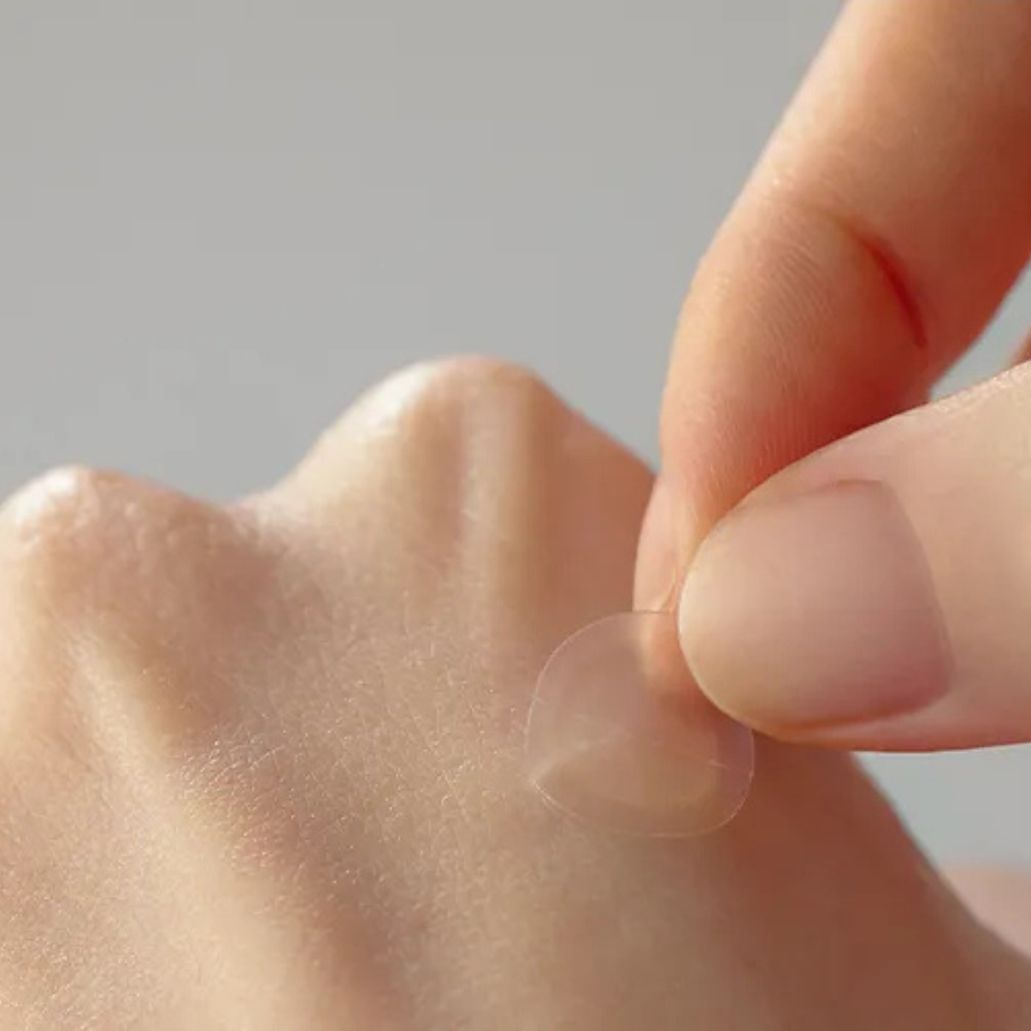 Hand applying a small SOME BY MI 30 Day Miracle Clear Spot Patch to the back of the hand against a neutral background