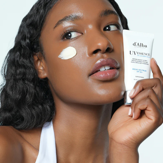 Woman applying d'Alba UV Essence sunscreen to her face with a white background