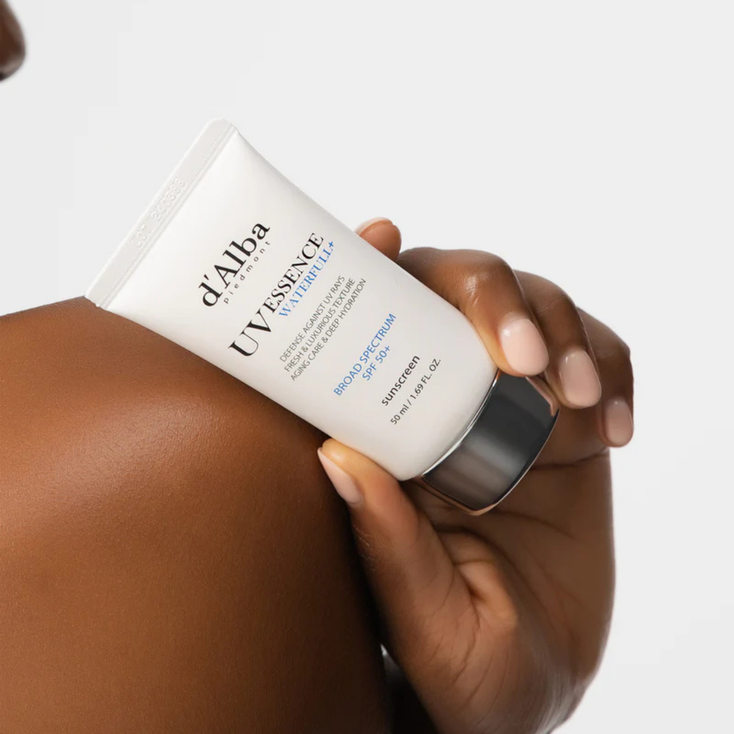 Hand holding a tube of d'Alba UV Essence Waterfull SPF 50+ PA++++ Sun Cream on skin