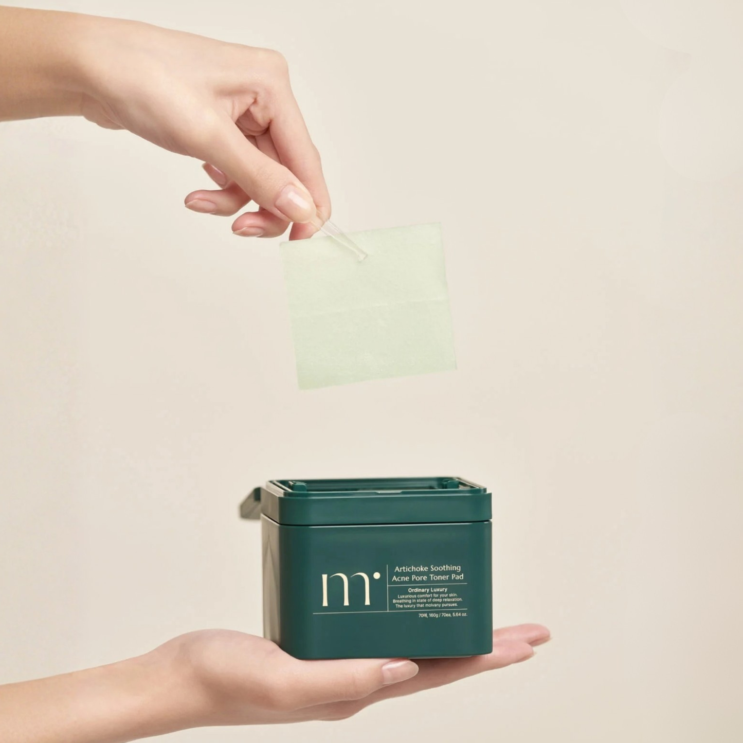 Hand holding a container of molvany Artichoke Soothing Acne Pore Toner Pads with another hand holding a forceps pinching a toner pad on a beige background
